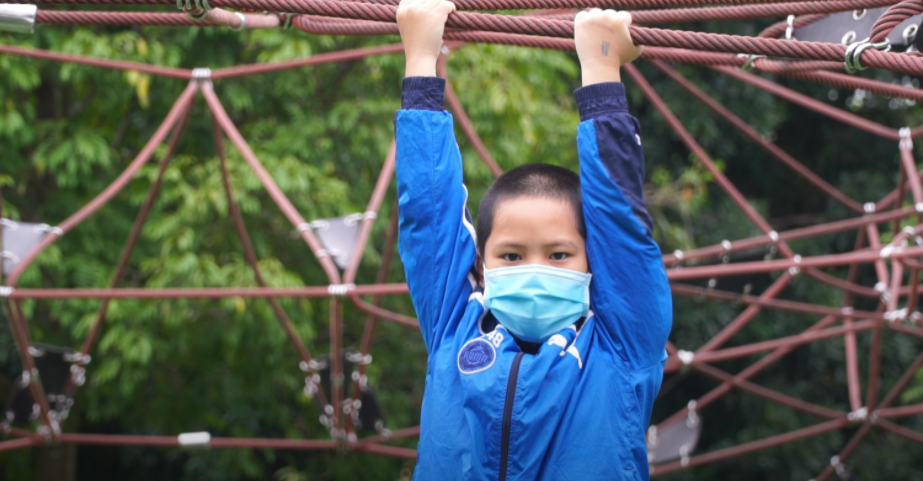 In Vietnam, a young boy wearing a medical mask hangs from monkey bars