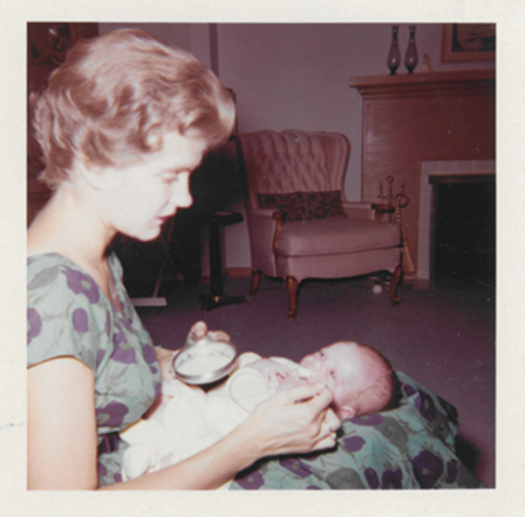 A scan of a film photo of Susan Skinner, she looks down at a small baby on her lap