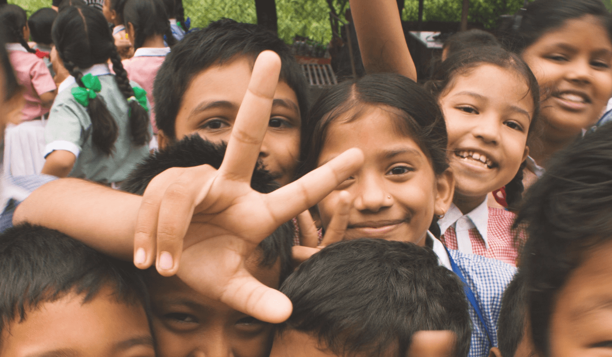 An energetic group of children smile, one holds up a peace sign