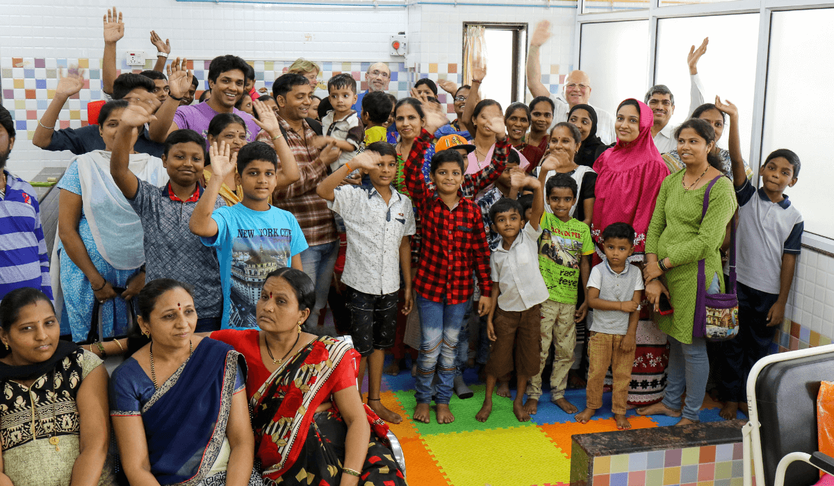 In Mumbai, a large group of people of all ages smile and wave